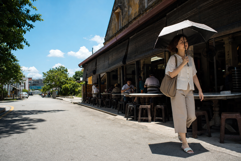 Woman with an umbrella under strong midday sun outside a kopitiam – SPF and PA